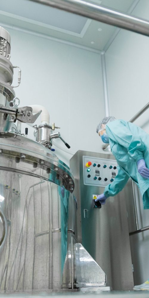pharmaceutical factory woman worker in protective clothing operating production line in sterile environment